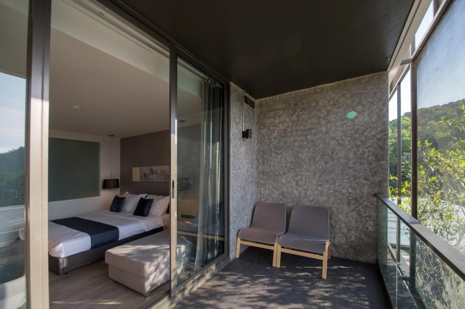 A modern bedroom with a large bed, a sofa, and a balcony with two chairs.
