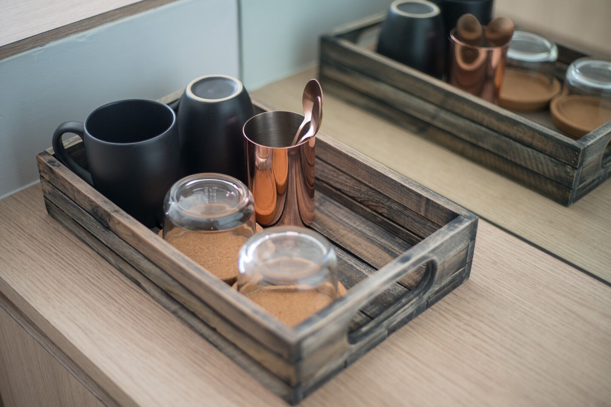 A wooden tray containing black and copper mugs, a glass jar, and a small container with a lid.