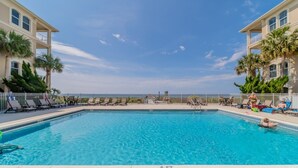 Una piscina rectangular con indicador de profundidad de 1.2 metros, rodeada de sillones de descanso y palmeras, con vista al océano al fondo.