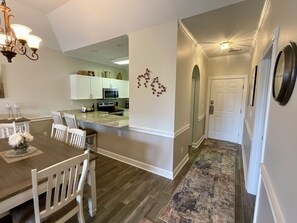 A modern kitchen with white cabinets, a granite countertop, and a dining area with a wooden table and white chairs. - 4737 Wild Iris Drive Magnolia Place 2 Bedroom Condo by RedAwning (Myrtle Beach)
