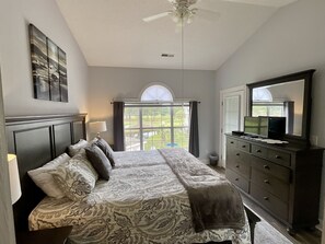A bedroom with a bed, a dresser, a television, and a window with a view of a garden. - 4737 Wild Iris Drive Magnolia Place 2 Bedroom Condo by RedAwning (Myrtle Beach)