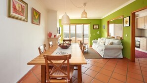 A dining area with a wooden table and chairs, a white sofa, and a kitchen visible through an open door. - CORAL VILLA, a charming landscape close to the beach, best choice for families (Carvoeira)