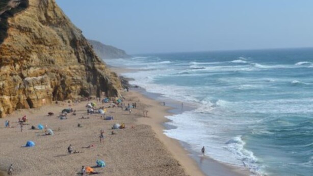 A beach with rocky cliffs, sandy shore, and umbrellas. - CORAL VILLA, a charming landscape close to the beach, best choice for families (Carvoeira)