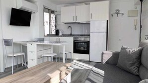 A compact kitchen with white cabinetry, a built-in oven, and a refrigerator. There is a dining area with a wooden table and two chairs. - Apartment with terrace just 250 m from the beach (Torre Del Mar)