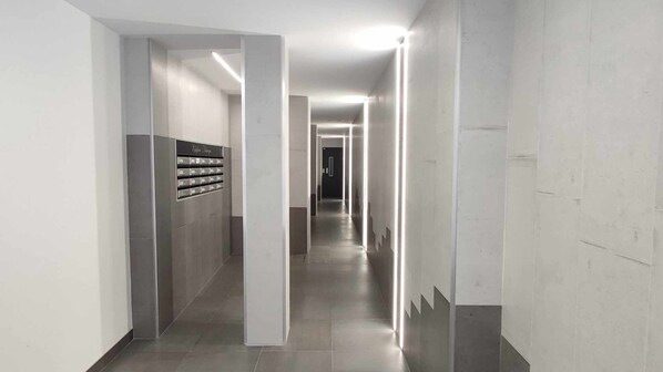 Un pasillo moderno y bien iluminado con varios casilleros en la pared izquierda y un camino recto que lleva a una puerta al final.