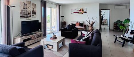 A modern living room with a flat-screen TV, two sofas, a coffee table, and a dining area with a bench.