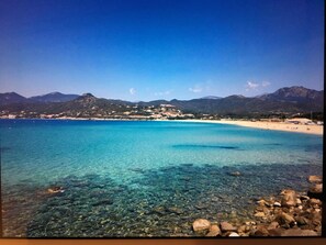Un paysage côtier avec une eau turquoise cristalline, une plage de sable et une ville en arrière-plan.