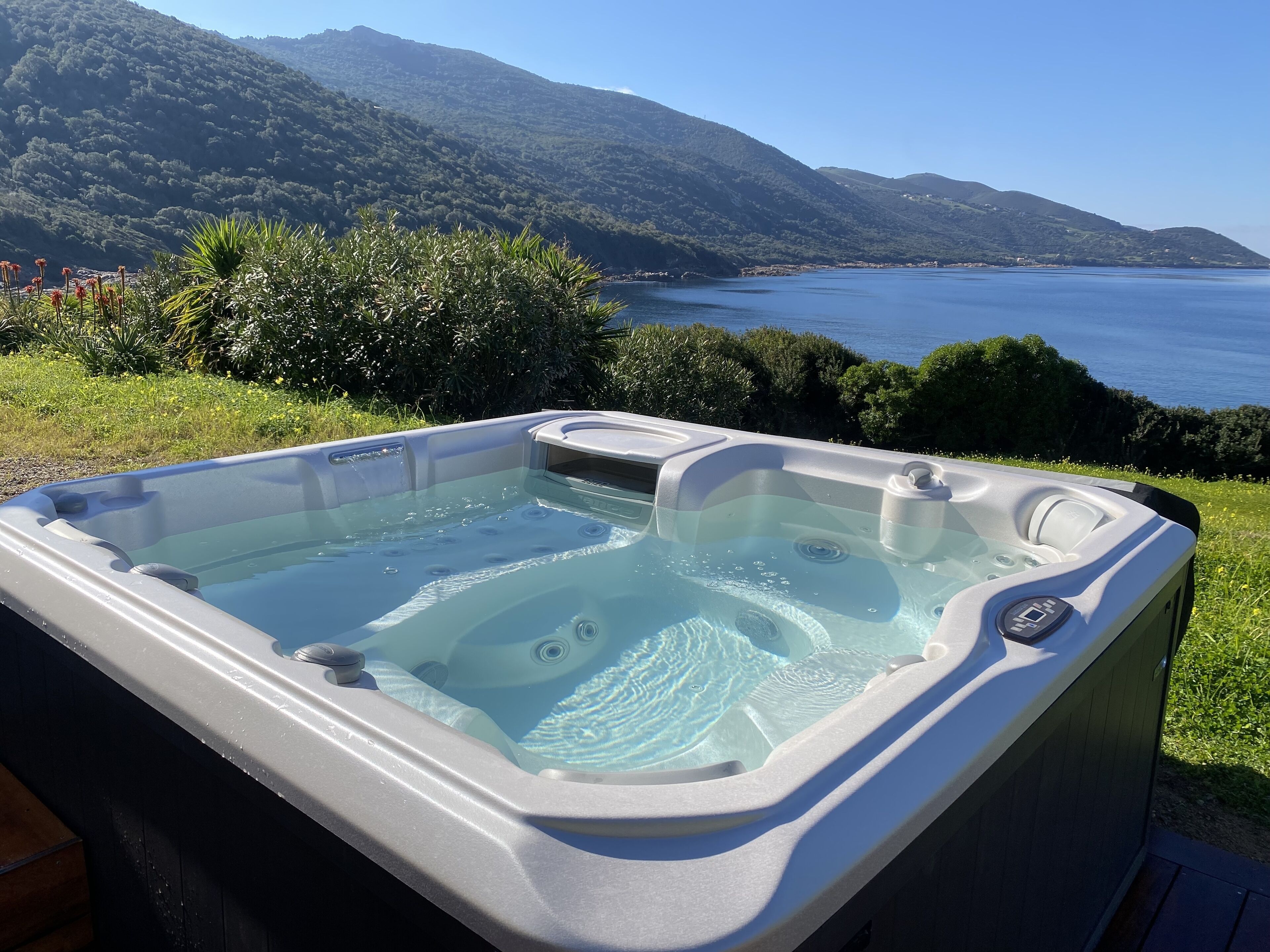 A hot tub with a clear view of a mountainous landscape and a body of water in the background.