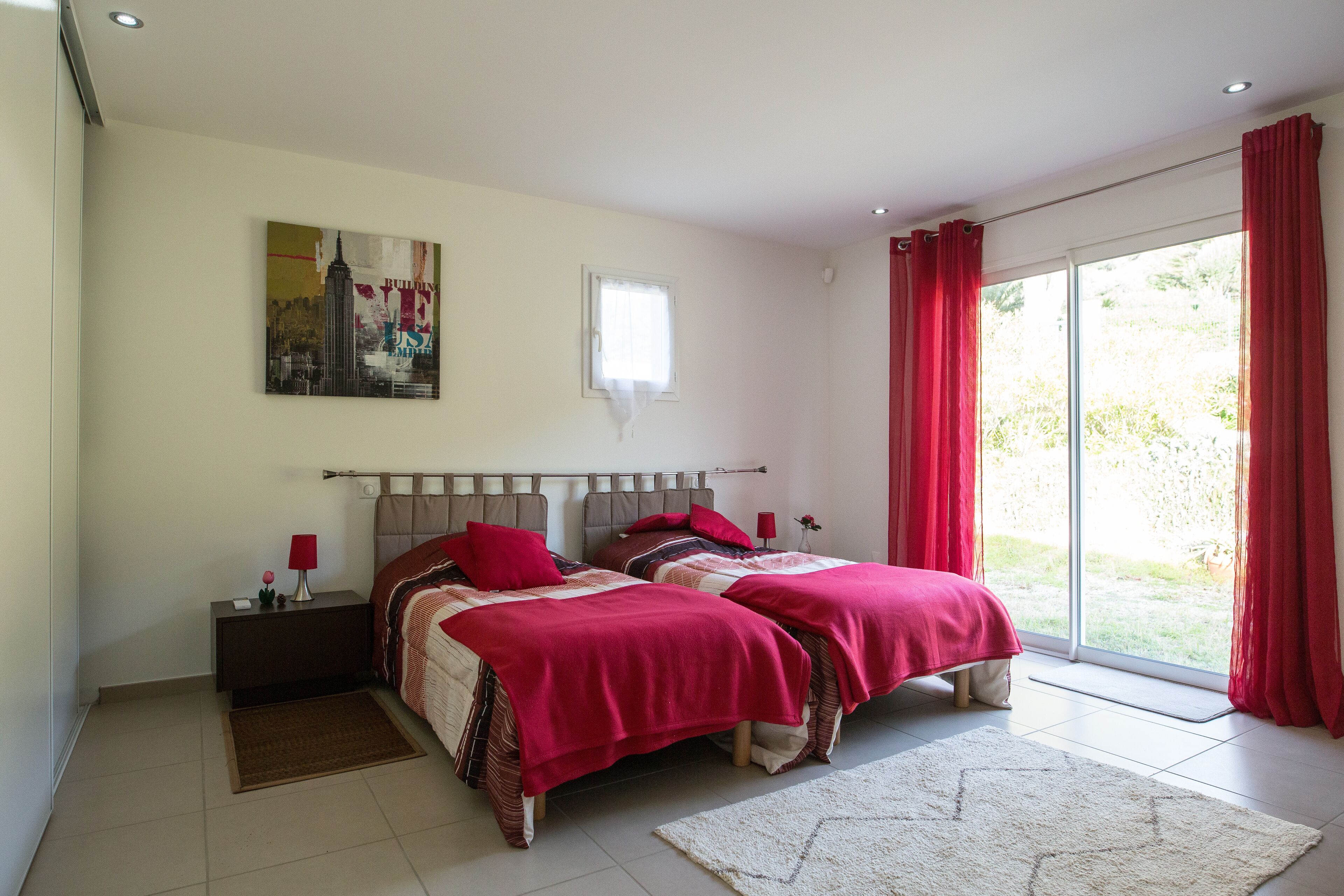 A bedroom with two beds, a nightstand, a window with curtains, and a painting on the wall.