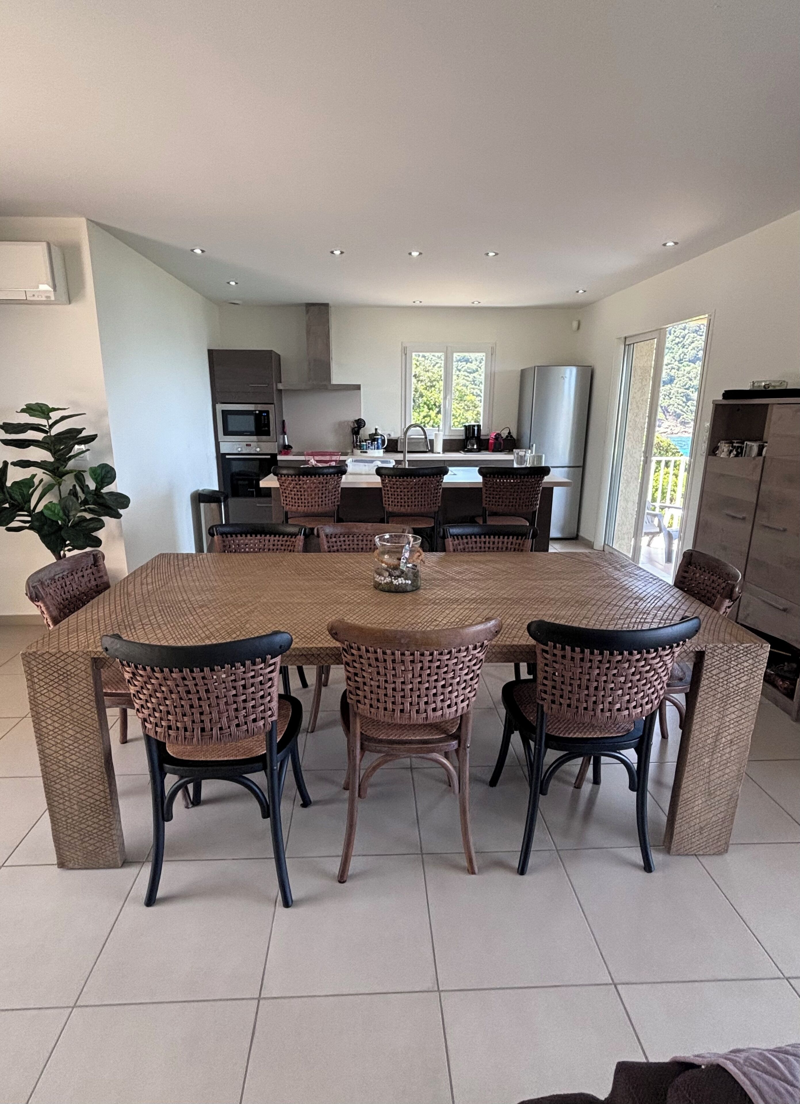 A modern kitchen with a central island, built-in appliances, and a large dining area with wicker chairs.