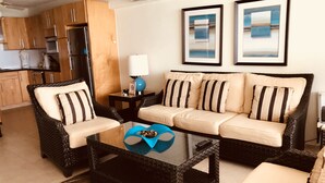 A living room with a sofa, chairs, a coffee table, and a kitchen in the background. -  Sunset Beach - Ocean front with stunning sea views, WI-FI, AC. (Oistins)