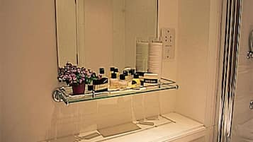 A bathroom with a large mirror, a glass shelf with toiletries, and a white sink with two towels.