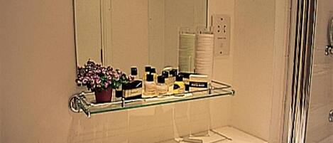 Une salle de bain avec un grand miroir, une étagère en verre où sont rangés les articles de toilette, et un lavabo blanc avec deux serviettes.