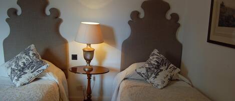 A hotel room with two beds, a table with a lamp, and a framed picture on the wall.