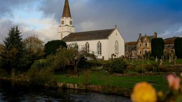 Een kerk met een opvallende toren en aangrenzende historische gebouwen, omgeven door een verzorgde tuin en een rivier.