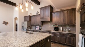 A kitchen with granite countertops, dark wooden cabinets, a stainless steel refrigerator, a coffee maker, and a toaster.
