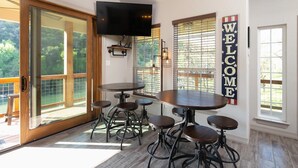 A dining area with a round table and stools, a TV mounted on the wall, and a 'WELCOME' sign.