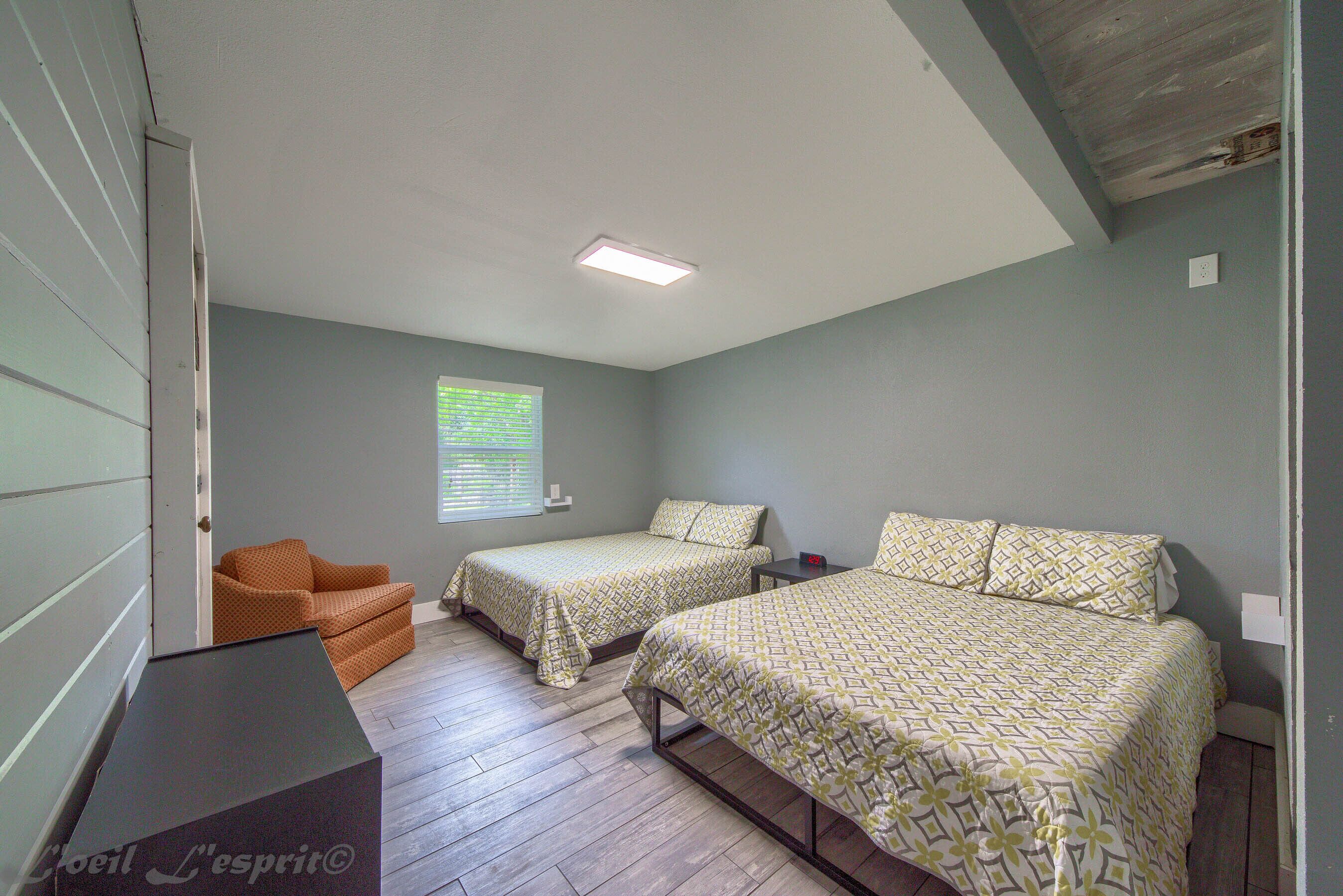 A bedroom with two beds, a chair, and a desk.