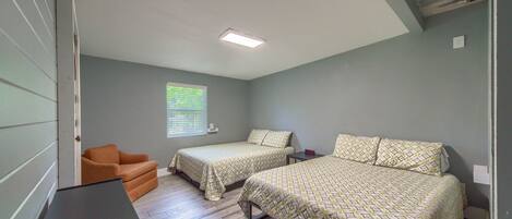 A bedroom with two beds, a chair, and a desk.