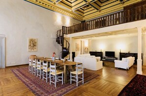 Amplia sala de estar con una mesa de comedor de madera, sofás blancos y una escalera que conduce a un nivel superior.