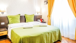 Une chambre d’hôtel avec un lit, une literie verte, une table de chevet, une lampe et une fenêtre avec des rideaux.
