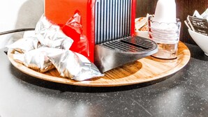 Une machine à expresso rouge, dotée d’une buse vapeur noire et d’une verseuse en verre, le tout posé sur un plateau en bois.