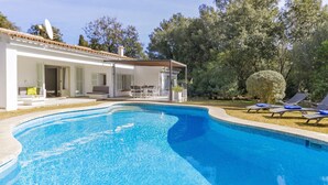 Una piscina con solárium, tumbonas y un edificio blanco de techado con tejas.
