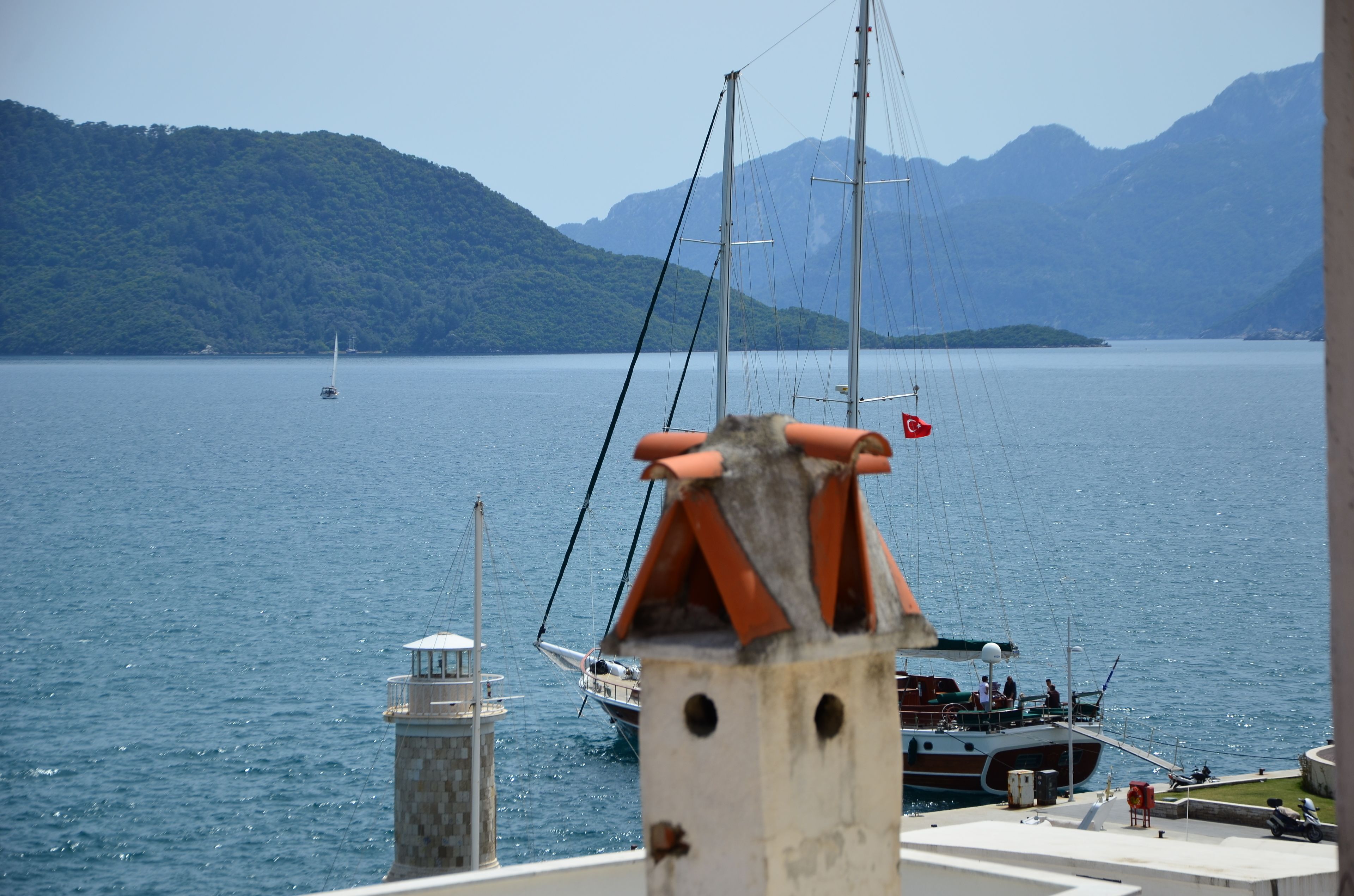 A coastal view with a lighthouse, a sailboat, and a mountainous backdrop.