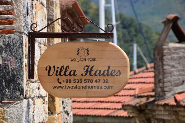 Un panneau en bois indiquant « Villa Hadès », avec les coordonnées et l’adresse du site web.