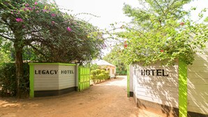 A dirt pathway leading to a hotel entrance with green gates and a sign reading "LEGACY HOTEL". - Legacy 2014 Hotel (Bondo)