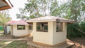 Two small, single-story buildings with red roofs, surrounded by trees and a grassy area. - Legacy 2014 Hotel (Bondo)