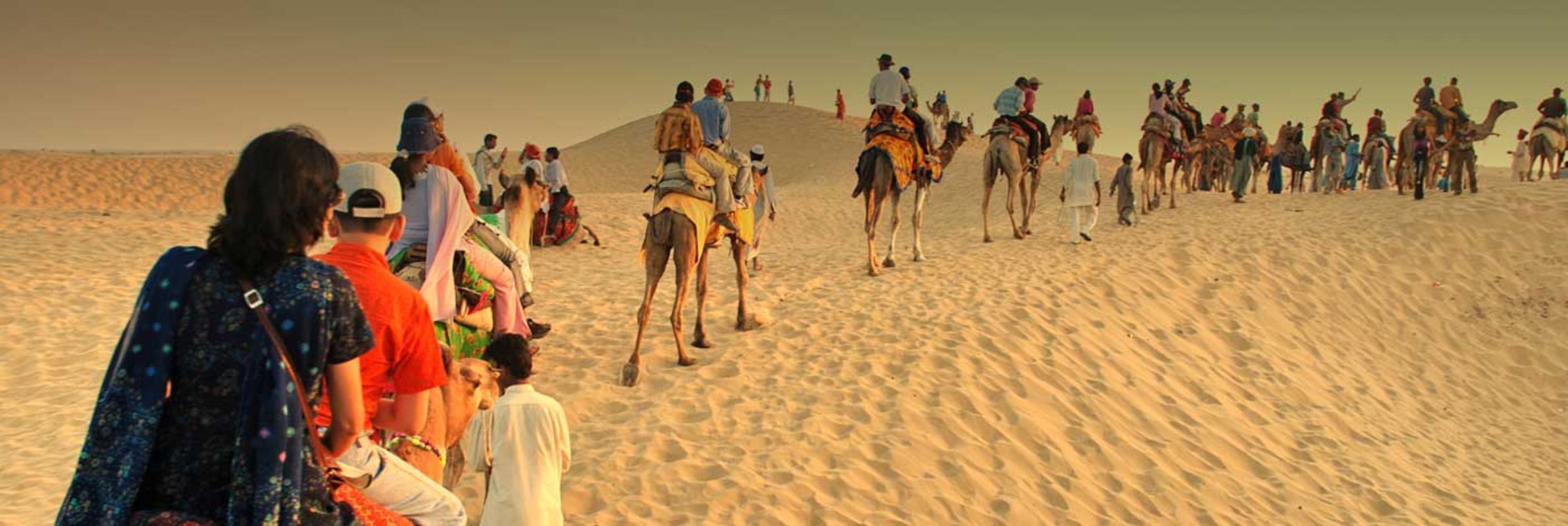 A group of people riding camels in a desert setting.