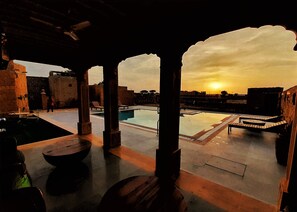 A rooftop pool area with stone pillars, a pool, and lounge chairs. - The Mamas Resort and Camp - Caters to Couples and Families (Jaisalmer)