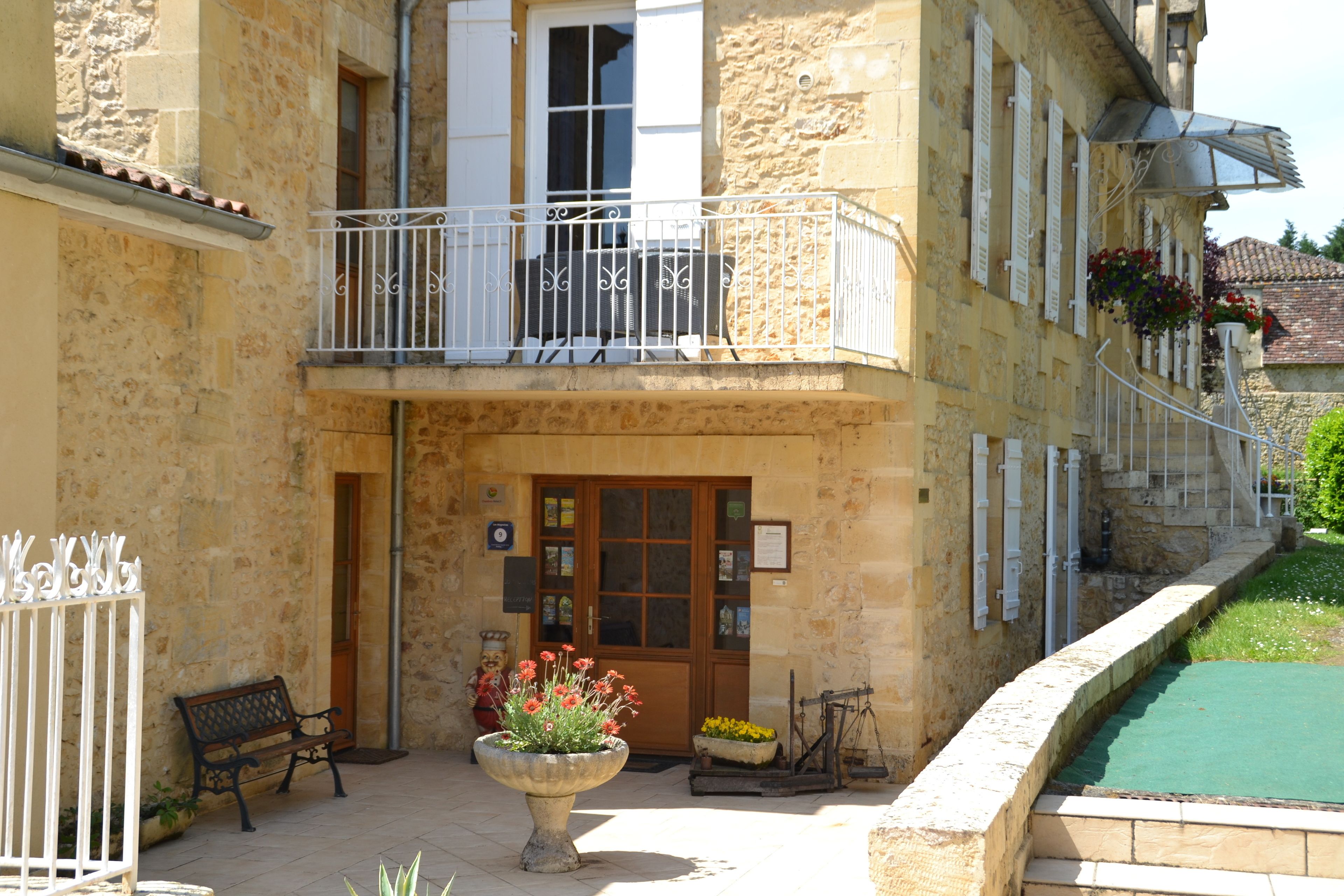 A stone building with a wooden door, a balcony with white railings, and a flower planter in front.