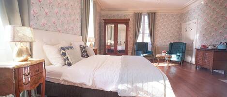 A bedroom with a large bed, a dresser, a chair, and a table.