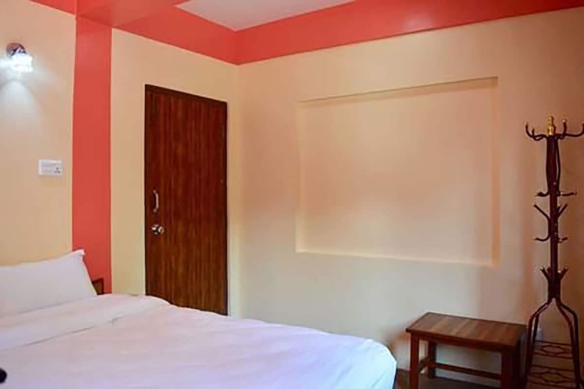 A bedroom with a bed, a wooden door, a small wooden table, and a coat rack.
