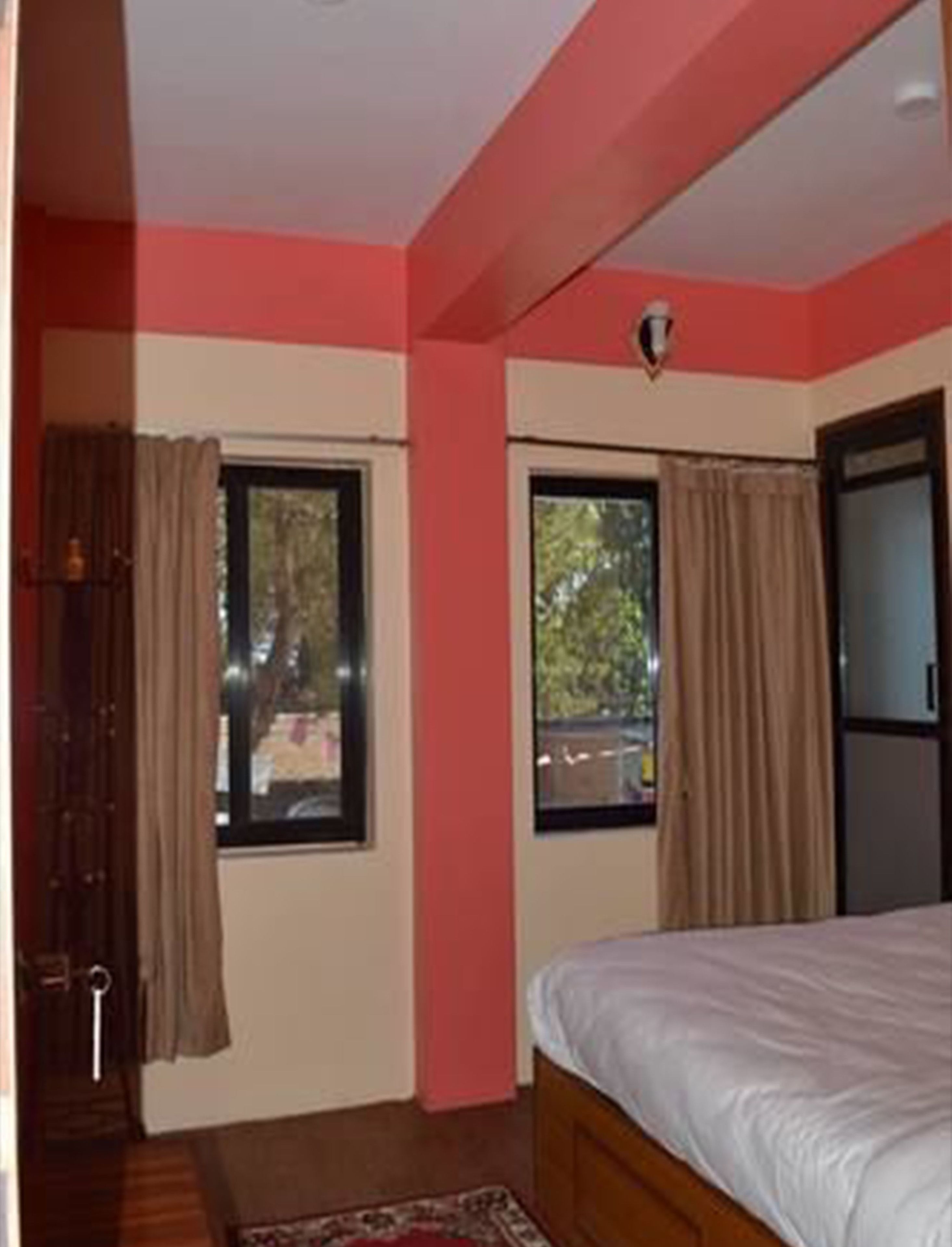 A bedroom with a bed, two windows with curtains, a door, and a small rug.