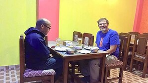 Deux personnes sont assises à une table à manger en bois, entourées de chaises.