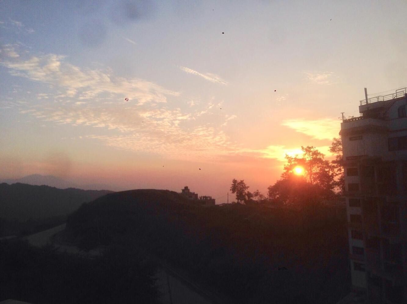 A sunset over a hilly landscape with a building in the foreground.