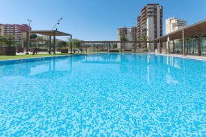 Ein Schwimmbecken mit Fliesenboden, umgeben von Bänken und einer Pergola.