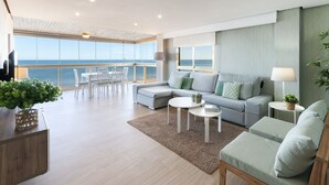Ein großzügiger Wohnbereich mit Balkon und Meerblick, ein graues Sofa, ein runder Couchtisch und ein Holzschrank.