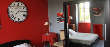 Una habitación de hotel con cama, una silla, una mesa, un reloj y un espejo.
