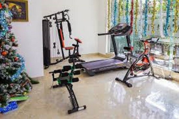 Une pièce équipée d’un tapis de course, d’un vélo d’appartement et d’un banc de musculation. On aperçoit un sapin de Noël dans un coin.