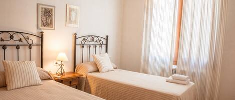 A hotel room with two beds, a nightstand with a lamp, and a window with curtains.