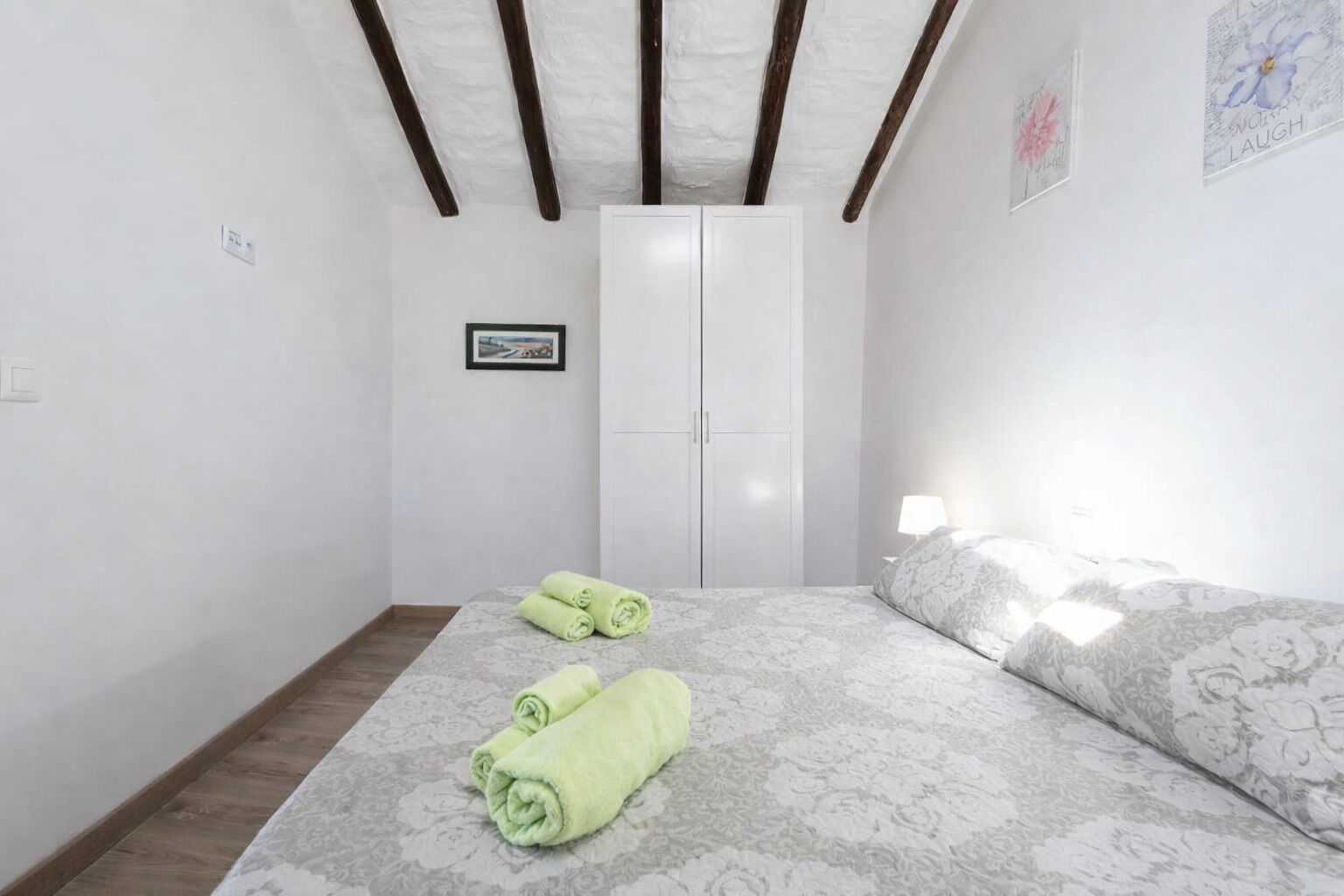 Un dormitorio con cama, armario, un cuadro en la pared y ventana.