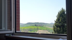 A view from a window overlooking a green landscape with a building in the distance. - Residence la Quiete (Guarene)