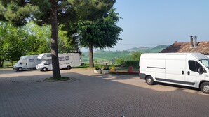 A parking area with a white van and a camper van, surrounded by trees and a view of hills. - Residence la Quiete (Guarene)