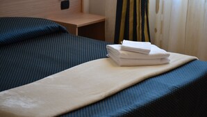 A neatly made bed with a blue and white striped bedspread, a beige blanket, and a stack of white towels. - Residence la Quiete (Guarene)