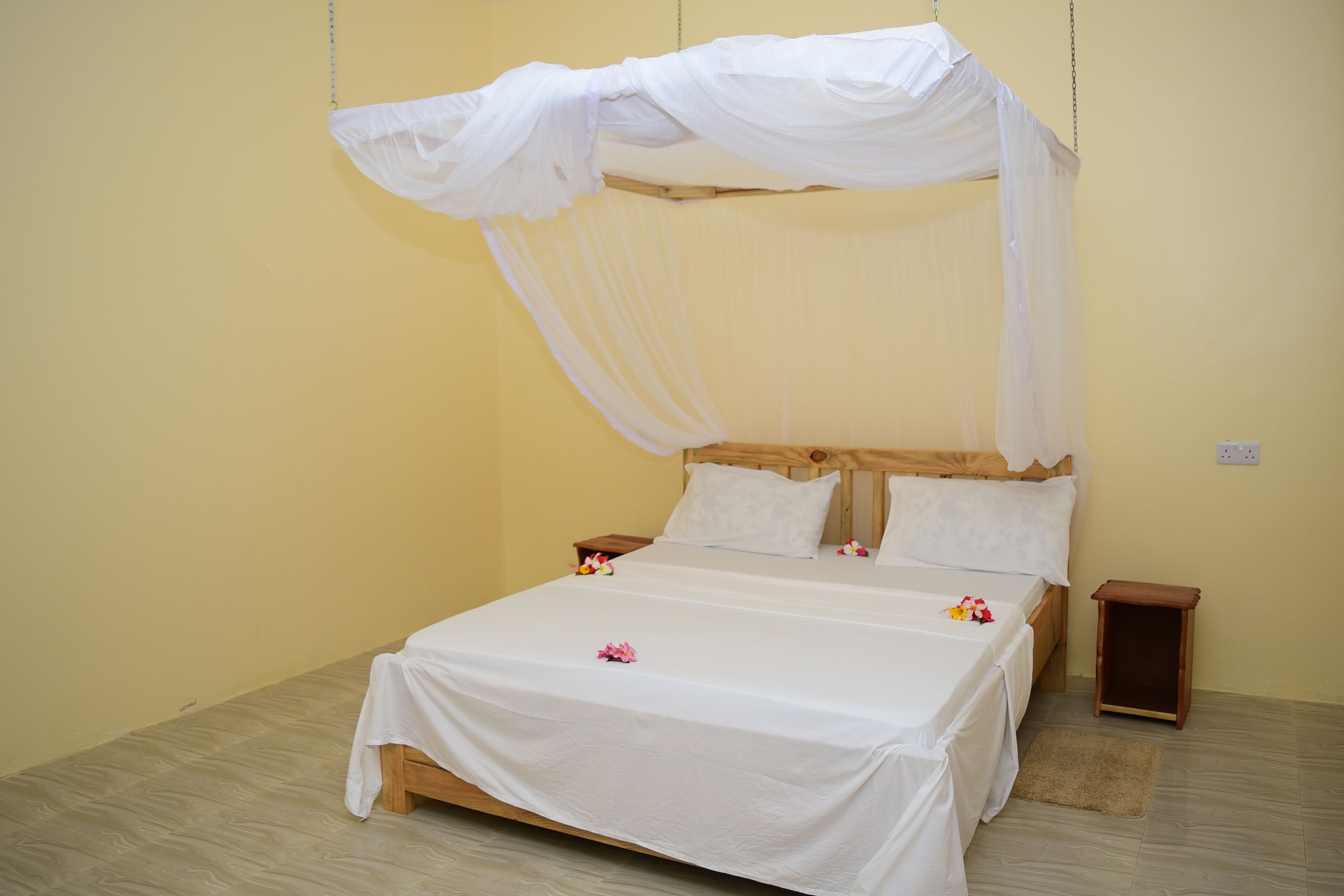 A single bed with a canopy, wooden headboard, and a bedside table with a lamp.