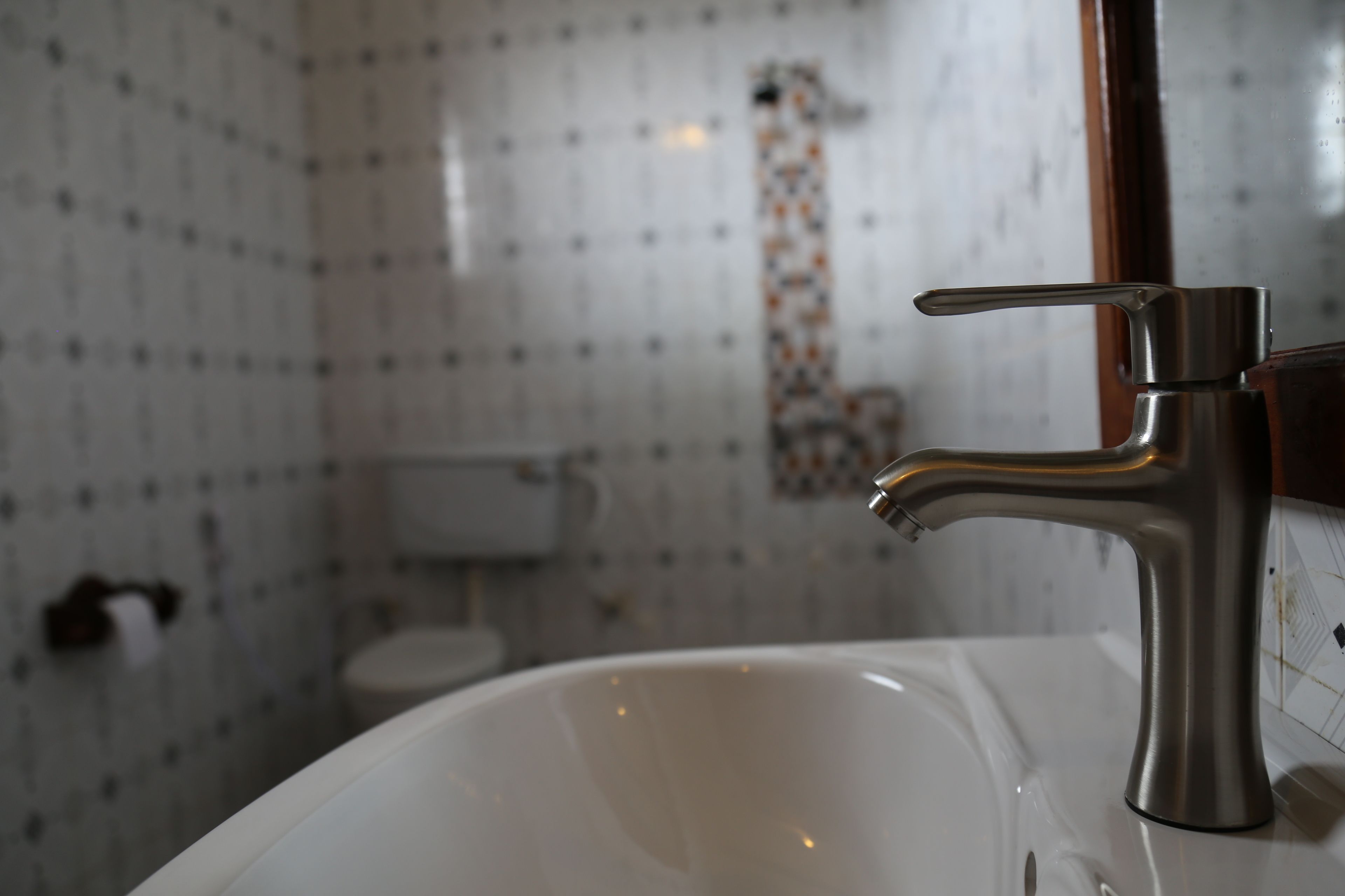A bathroom with a white sink, a chrome faucet, and a tiled wall.